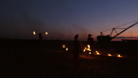 Feuershow:-Drei-Frauen-In-Ihren-Händen-Drehen-Brennende-Speere-Und-Fächer-Im-Sand-Mit-Einem-Mann-Mit-Zwei-Flammenwerfern-In-Zeitlupe